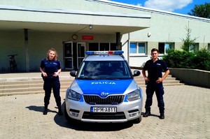 policjant i policjantka stoją przy radiowozie