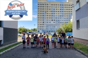Policjanci z grupą dzieci i psem służbowym pozują do zdjęcia.