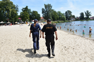 Policjantka i strażak idą wzdłuż plaży.
