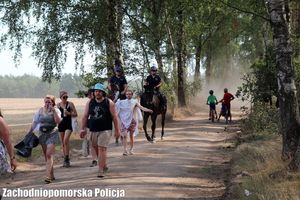 dwaj policjanci na koniach i uczestnicy festiwalu idący drogą