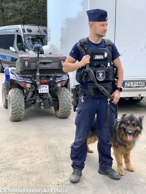 policjant z psem służbowym na smyczy, w tle pojazdy policyjne