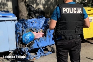 na zdjęciu policjant, w tle nadpalony kontener na śmieci