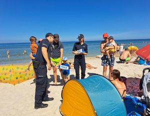Policjanci rozdają ulotki informacyjne wypoczywającym na plaży ludziom.