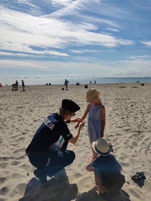 Policjantka na plaży zakłada na rękę opaskę dziewczynce.