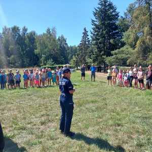 Policjantka na polanie leśnej rozmawia z uczestnikami obozu harcerskiego.