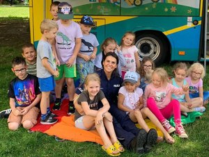 Policjantka z grupą dzieci siedzi na trawie pozując do zdjęcia.