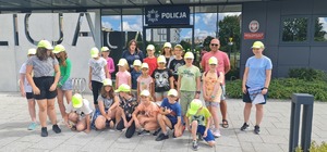 Policjantka pozuje do zdjęcia z dziećmi i ich opiekunami w tle budynek Komendy Powiatowej Policji w Skarżysku - Kamiennej.