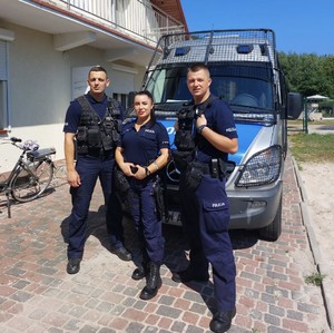 Troje policjantów stoi przed radiowozem