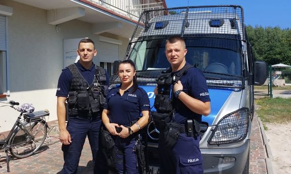 Troje policjantów stoi przed radiowozem