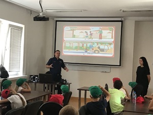 Policjant prezentuje, siedzącym przed nim dzieciom, zasady bezpiecznych zachowań.