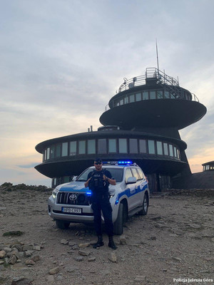 policjant stoi przy radiowozie zaparkowanym przy szczycie Śnieżki