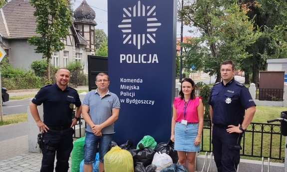 Policjanci i tata chłopca przy zebranych nakrętkach przez budynkiem komendy