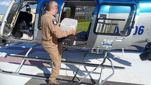 Policyjny lotnik wkładający pojemnik do transportowania organów do śmigłowca.