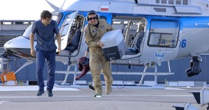 Mężczyzna w niebieskim uniformie medycznym i policyjny pilot niosący pojemnik na organy oddalają się od widocznego za nimi śmigłowca.