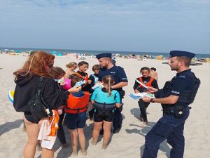 Policjanci rozdają na plaży ulotki dotyczące bezpiecznych zachowań.