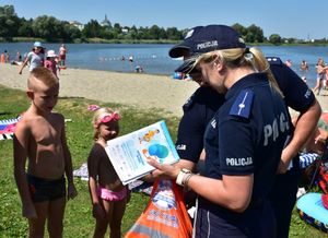 Policjanci na plaży rozdają ulotki i gadżety promujące bezpieczne zachowania nad wodą.