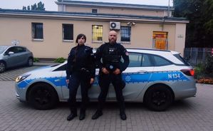 policjant i policjantka stoją przed radiowozem policyjnym