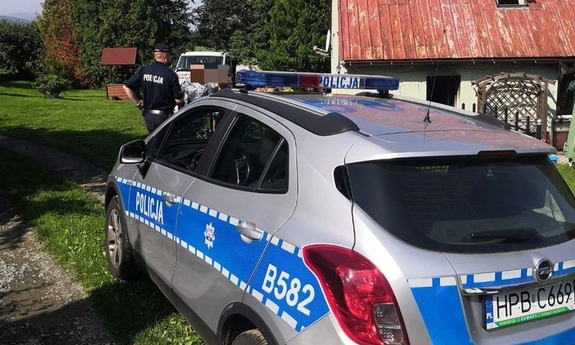 Na zdjęciu widać policjanta, który stoi obok radiowozu. W tle budynek, w którym doszło do pożaru