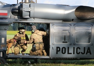 Dwaj mężczyźni w umundurowaniu taktycznym i policyjny pies na pokładzie śmigłowca.