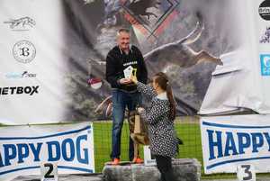 kobieta wręcza mężczyźnie stojącemu na podium razem z psem statuetkę