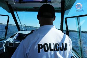 Policjant odwrócony tyłem steruje łodzią policyjną.