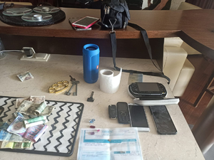 na stole leżą zabezpieczone przez policjantów drobne przedmioty między innymi telefony komórkowe, kilka banknotów, klucze, kastet, kluczyki do samochodu i głośnik bluetooth