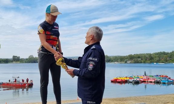 Komendant policji wręcza puchar stojącej na podium policjantce w stroju sportowym