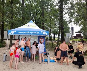 Uczestnicy wydarzenia stoją przy namiocie obok straż pożarna prezentuje zasady pierwszej pomocy.