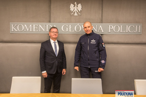 Spotkanie Zastępcy Komendanta Głównego Policji z Ambasadorem RP w Katarze: od lewej stoi Ambasador w garniturze, a obok niego wiceszef Policji w mundurze. W tle widoczna jest ścianka z napisem Komenda Główna Policji