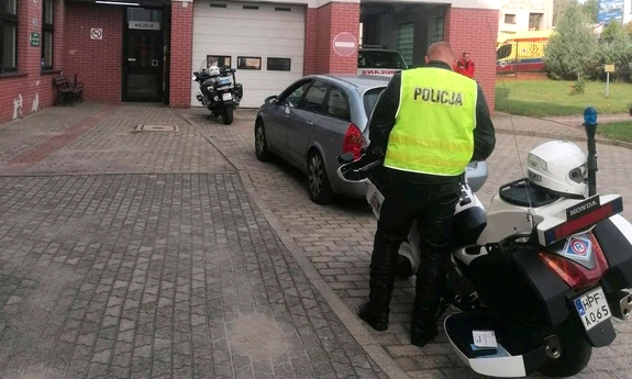 stojące przed szpitalem dwa motocykle policyjne i umundurowany policjant