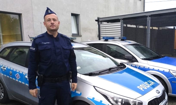 Umundurowany policjant stoi przy radiowozach