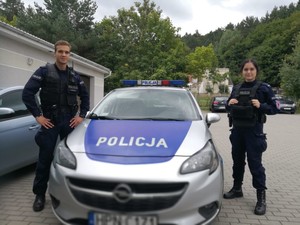 dwoje umundurowanych policjantów stoi przy radiowozie