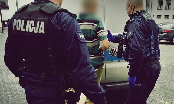 dwaj policjanci z zatrzymanym mężczyzną przy radiowozie