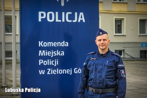 Policjant na tle logo Komendy Miejskiej Policji w Zielonej Górze