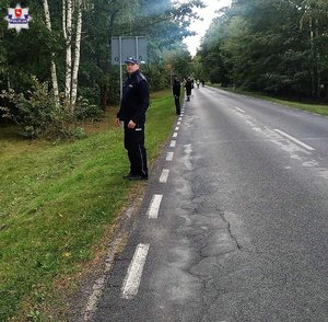 umundurowani funkcjonariusze stoją na drodze na skraju lasu