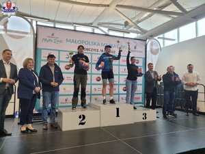 trzy policjantki w strojach sportowych na podium wyścigu kolarskiego, obok podium stoją inne osoby