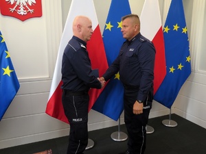 Gen. insp. Jarosław Szymczyk ściska dłoń w geście gratulacji umundurowanemu policjantowi. W tle flagi: polska i UE