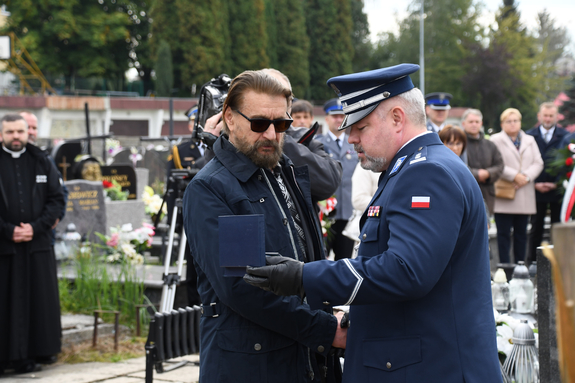 oficer Policji wręcza mężczyźnie odznaczenie, z tyłu widać zebranych ludzi