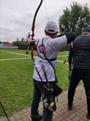 Sierżant Adam Ścibski podczas swojej próby trzyma łuk w lewej ręce, a prawą napina cięciwę z założona strzałą. Ujęcie od tyłu