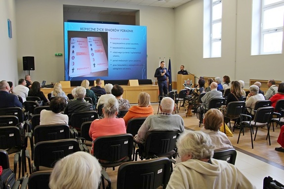 Konferencja dla seniorów w auli w Komendzie Wojewódzkiej Policji w Poznaniu. Widok z tyłu na siedzących na auli ludzi