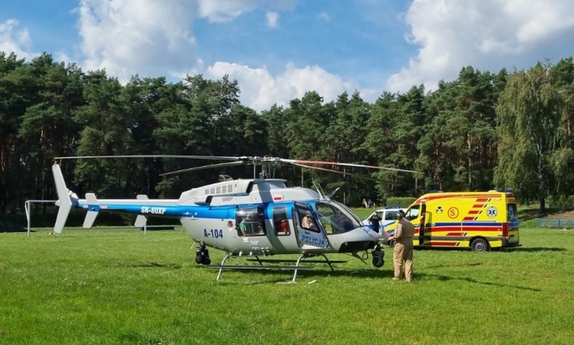 Policyjny Bell 407 GXi na płycie boiska, drugi plan – karetka pogotowia, trzeci plan – radiowóz policyjny