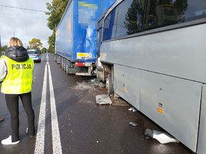 Tył samochodu ciężarowego, a za nim autobus i policjant