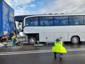 Uszkodzony samochód ciężarowy, a za nim uszkodzony autobus oraz policjant