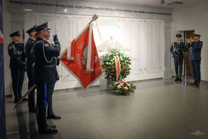 przed odsłoniętą tablica pamięci widać wieńce z kwiatów. Z lewej strony stoi poczet sztandarowy Policji, z prawej umundurowany policjant gra na trąbce