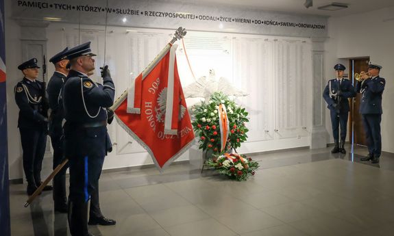 przed odsłoniętą tablica pamięci widać wieńce z kwiatów. Z lewej strony stoi poczet sztandarowy Policji, z prawej umundurowany policjant gra na trąbce