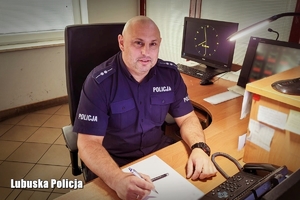umundurowany policjant siedzi przy biurku, w ręku trzyma długopis