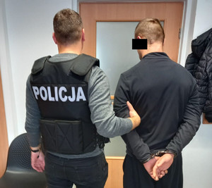 policjant trzyma zatrzymanego skutego kajdankami