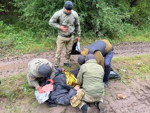 trzej mężczyźni udzielają pomocy leżącemu na ziemi rannemu mężczyźnie. Czwarty funkcjonariusz stoi przy nich i trzyma w ręku torbę