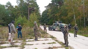 funkcjonariusze i wojskowi z bronią rozstawieni na terenie leśnym. Z tyłu widać wojskowy pojazd
