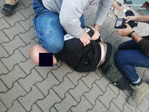 Dwóch policjantów po cywilnemu obezwładniło na chodniku podejrzanego - łysego mężczyznę. Policjant po prawej przeszukuje jego rzeczy